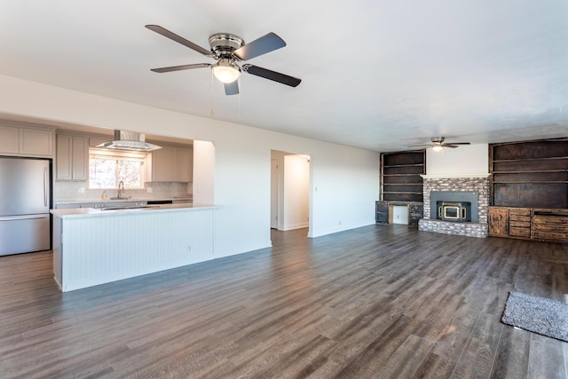 unfurnished living room with ceiling fan, a brick fireplace, built in shelves, and dark wood-type flooring