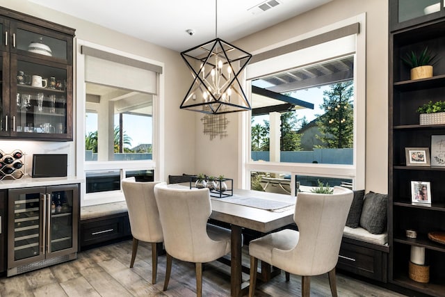 dining room featuring indoor bar, an inviting chandelier, light hardwood / wood-style flooring, and beverage cooler