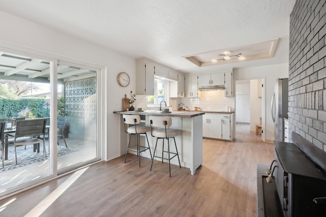 kitchen with white cabinetry, a tray ceiling, a wealth of natural light, a kitchen bar, and kitchen peninsula