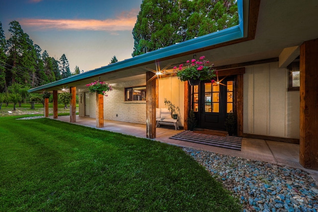 exterior entry at dusk featuring a yard and a patio area