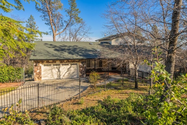 view of front of home featuring driveway, stone siding, a fenced front yard, and a garage