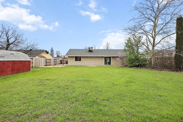 back of property with an outbuilding, a yard, and fence