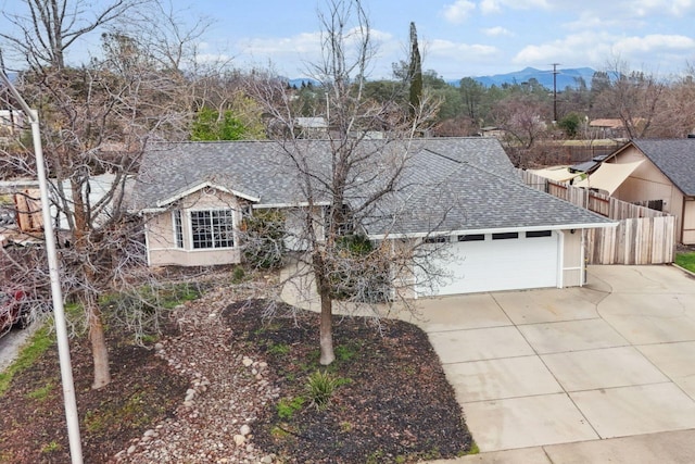 ranch-style house with a mountain view, a garage, a shingled roof, fence, and concrete driveway