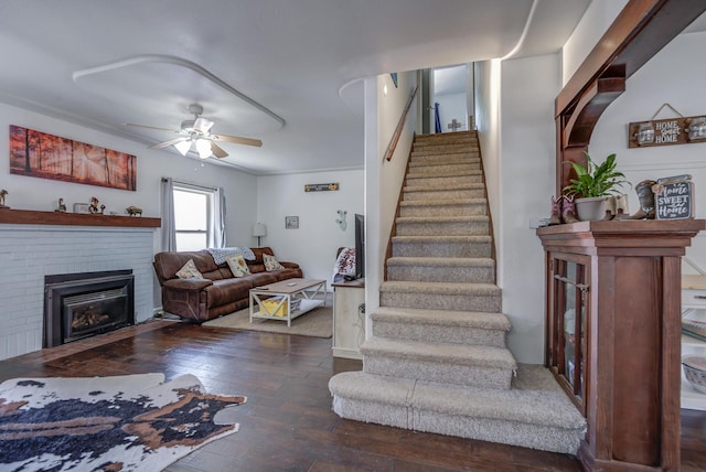 stairway with a brick fireplace, ornamental molding, hardwood / wood-style floors, and ceiling fan