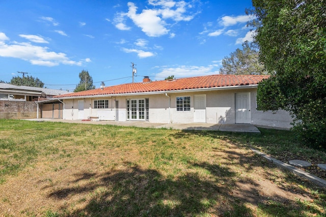 rear view of house featuring a tile roof, a chimney, a lawn, a patio, and stucco siding