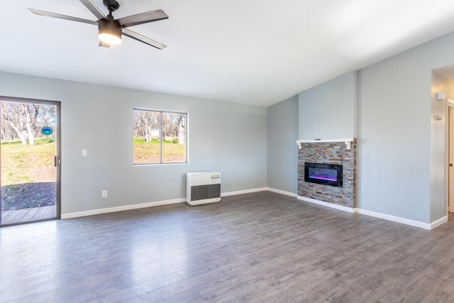 unfurnished living room with a stone fireplace, dark hardwood / wood-style floors, heating unit, and ceiling fan