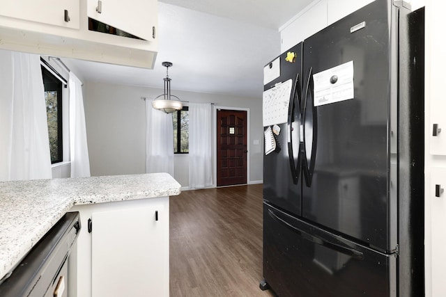 kitchen with black refrigerator, hanging light fixtures, light stone countertops, white cabinets, and dark hardwood / wood-style flooring