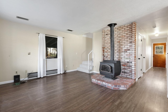 unfurnished living room with a wood stove, dark wood-type flooring, and a textured ceiling