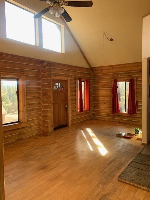 unfurnished living room featuring wood-type flooring, ceiling fan, log walls, and high vaulted ceiling