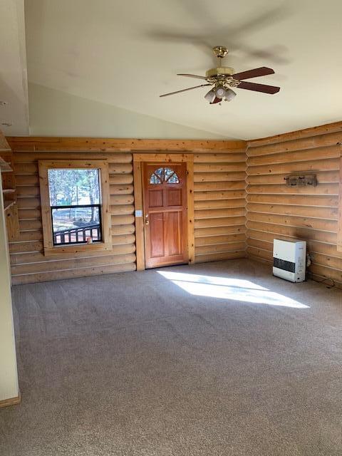 unfurnished living room featuring lofted ceiling, ceiling fan, rustic walls, and carpet