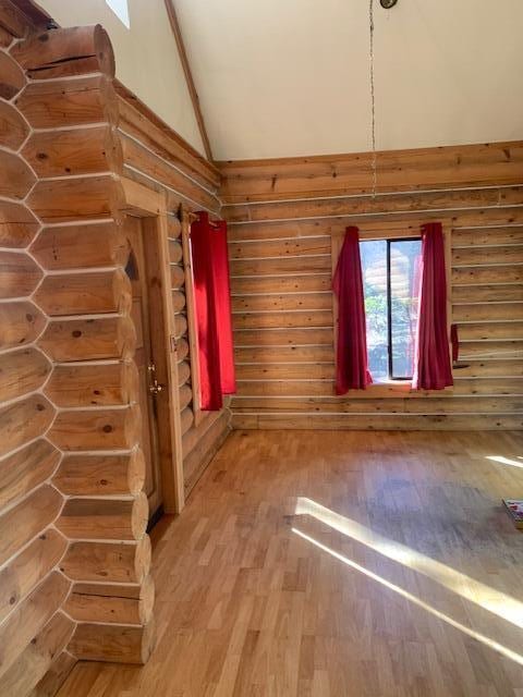 empty room featuring hardwood / wood-style floors, high vaulted ceiling, and rustic walls