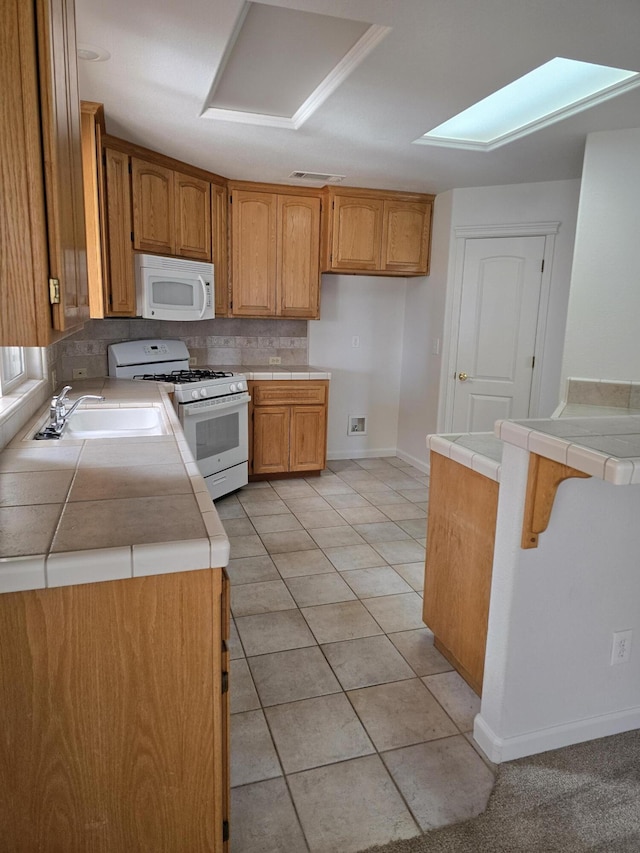 kitchen featuring sink, white appliances, light tile patterned floors, a skylight, and tile countertops