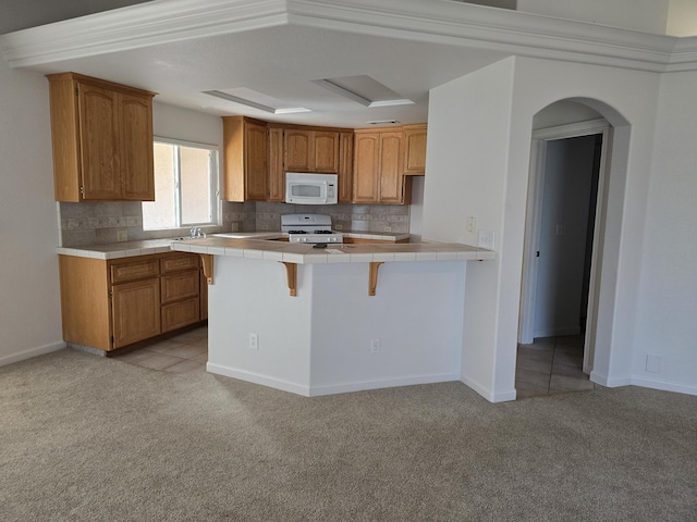 kitchen featuring a kitchen bar, light carpet, tile counters, white appliances, and decorative backsplash