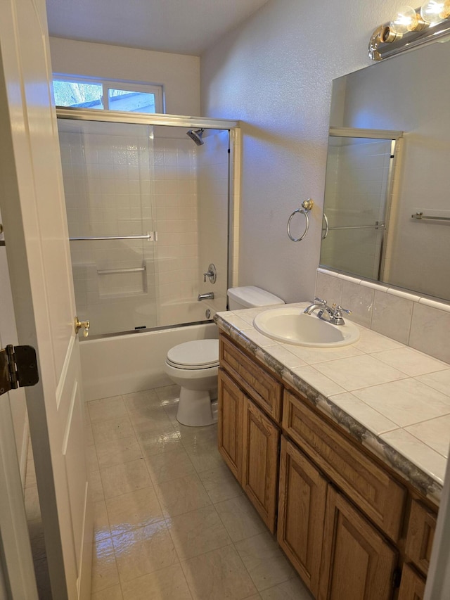 full bathroom with vanity, bath / shower combo with glass door, tile patterned floors, and toilet