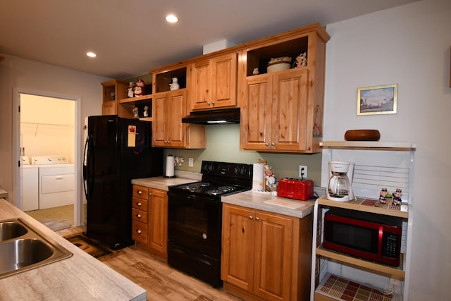 kitchen with sink, washing machine and dryer, light hardwood / wood-style flooring, and black appliances