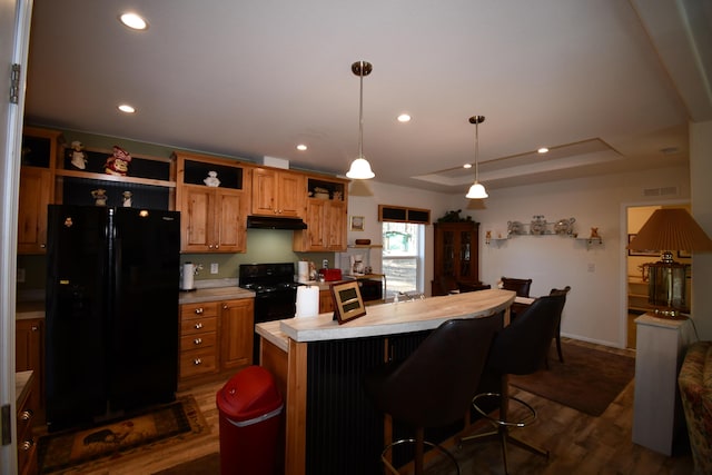 kitchen featuring a tray ceiling, dark hardwood / wood-style floors, pendant lighting, a kitchen island with sink, and black appliances