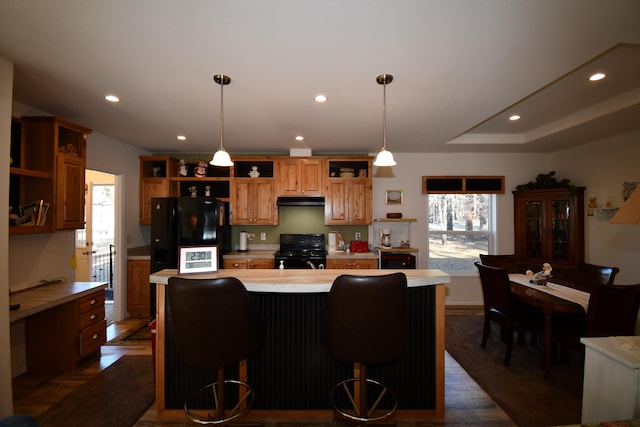 kitchen featuring a kitchen bar, hanging light fixtures, a kitchen island, and black appliances