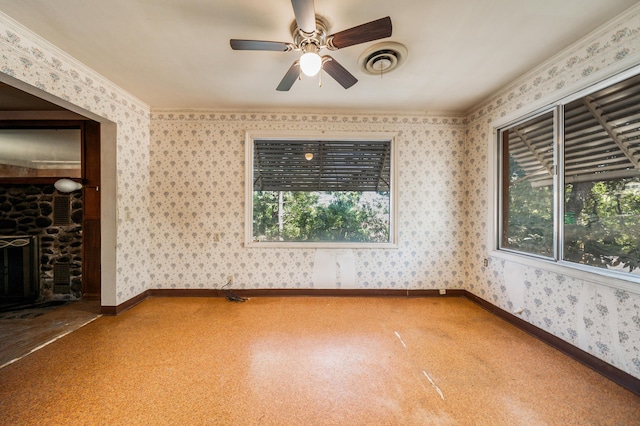 spare room with ceiling fan, ornamental molding, and a stone fireplace