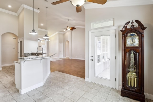 kitchen featuring hanging light fixtures, a kitchen breakfast bar, high vaulted ceiling, light stone counters, and ornamental molding