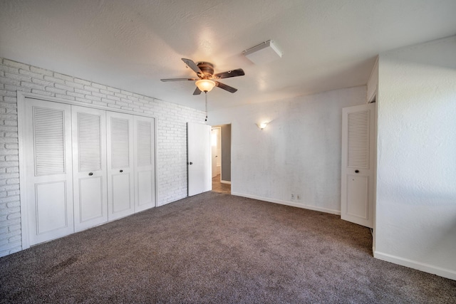 unfurnished bedroom featuring ceiling fan, a textured ceiling, brick wall, dark carpet, and a closet