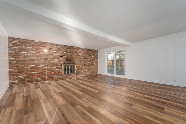 unfurnished living room with beamed ceiling, brick wall, a fireplace, and hardwood / wood-style floors