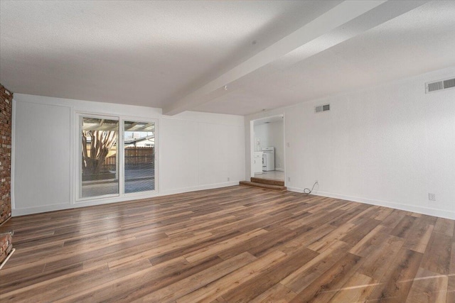 unfurnished living room featuring beamed ceiling, washer / dryer, a textured ceiling, and dark hardwood / wood-style flooring