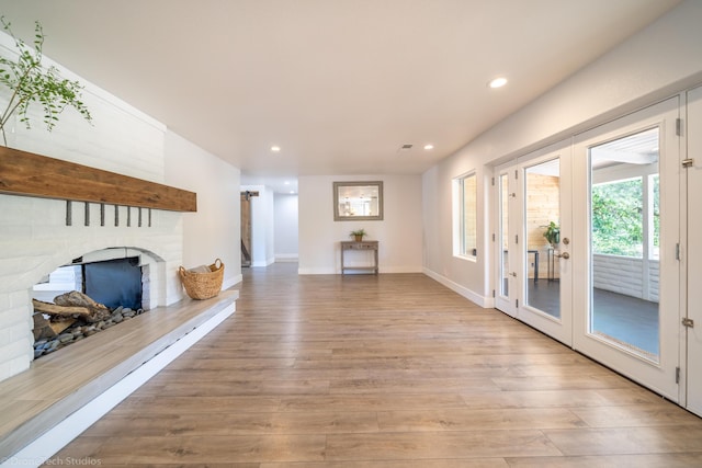 unfurnished living room featuring a brick fireplace, light hardwood / wood-style floors, and french doors