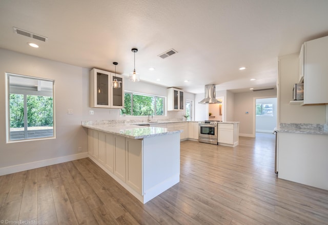 kitchen with island range hood, stainless steel stove, white cabinets, hanging light fixtures, and kitchen peninsula