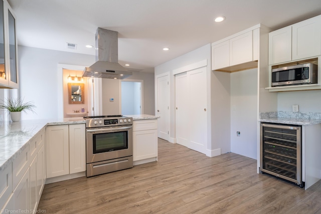 kitchen with white cabinetry, stainless steel appliances, island range hood, light stone countertops, and beverage cooler