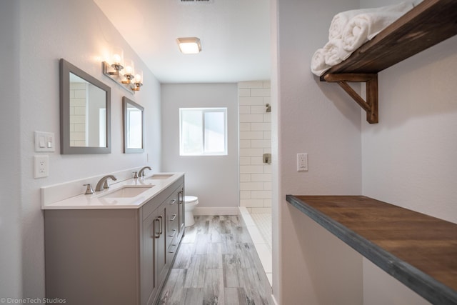 bathroom with hardwood / wood-style flooring, tiled shower, vanity, and toilet