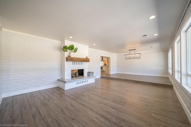 unfurnished living room with wood-type flooring, ornamental molding, a large fireplace, and brick wall