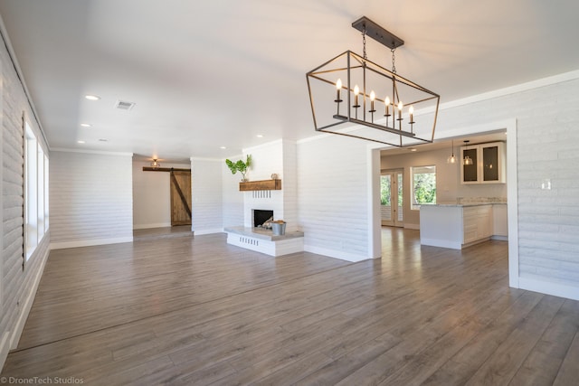 unfurnished living room with brick wall, dark hardwood / wood-style floors, ornamental molding, a barn door, and a brick fireplace