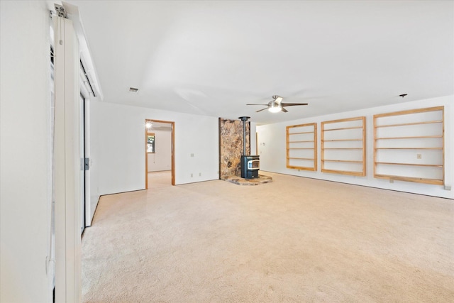 unfurnished living room featuring light colored carpet, ceiling fan, and a wood stove