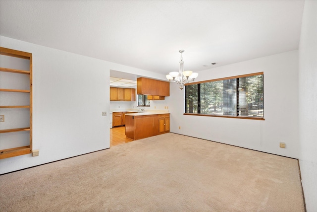 kitchen with sink, an inviting chandelier, decorative light fixtures, light colored carpet, and kitchen peninsula