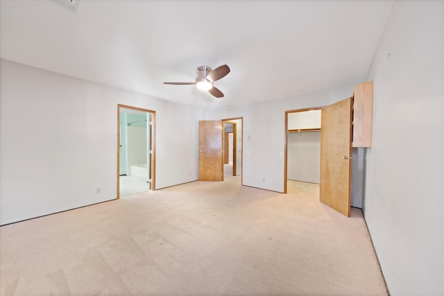 unfurnished bedroom featuring ensuite bath, a walk in closet, light colored carpet, a closet, and ceiling fan