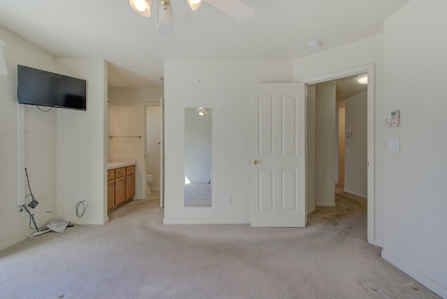 unfurnished bedroom featuring ceiling fan, ensuite bathroom, and light colored carpet