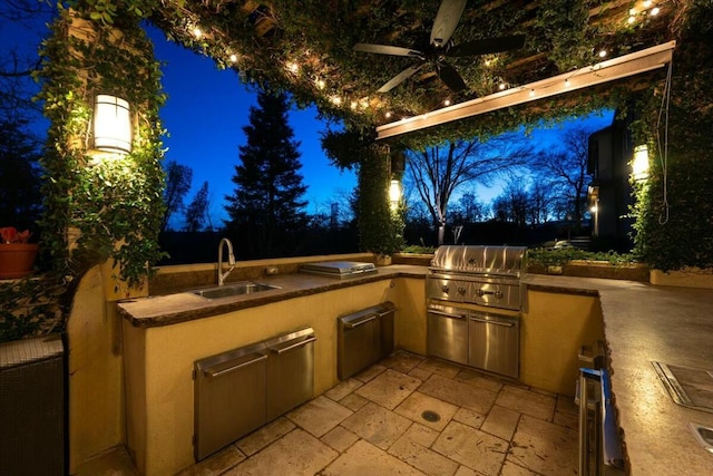 patio at twilight with a grill, an outdoor kitchen, sink, and ceiling fan