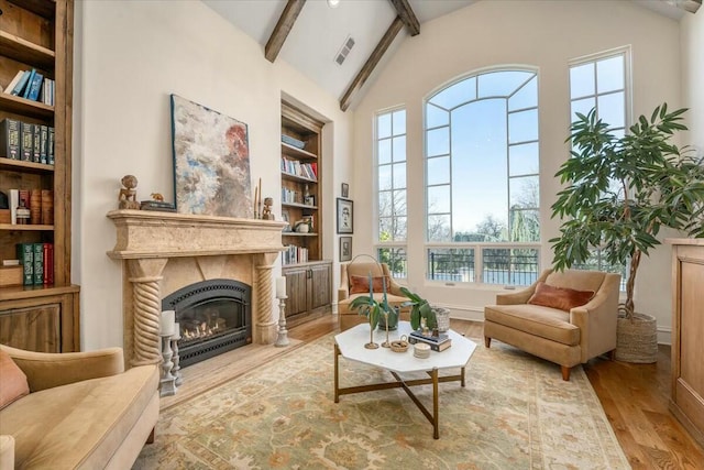 living area featuring beamed ceiling, a healthy amount of sunlight, a high end fireplace, and light hardwood / wood-style floors