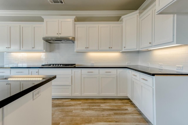 kitchen with ornamental molding, white cabinets, stainless steel gas stovetop, light hardwood / wood-style floors, and backsplash