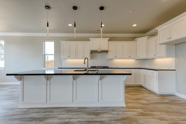 kitchen with sink, white cabinets, hanging light fixtures, a center island with sink, and light wood-type flooring