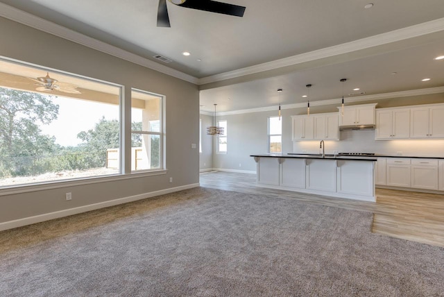 kitchen with crown molding, ceiling fan, white cabinetry, a center island with sink, and decorative light fixtures