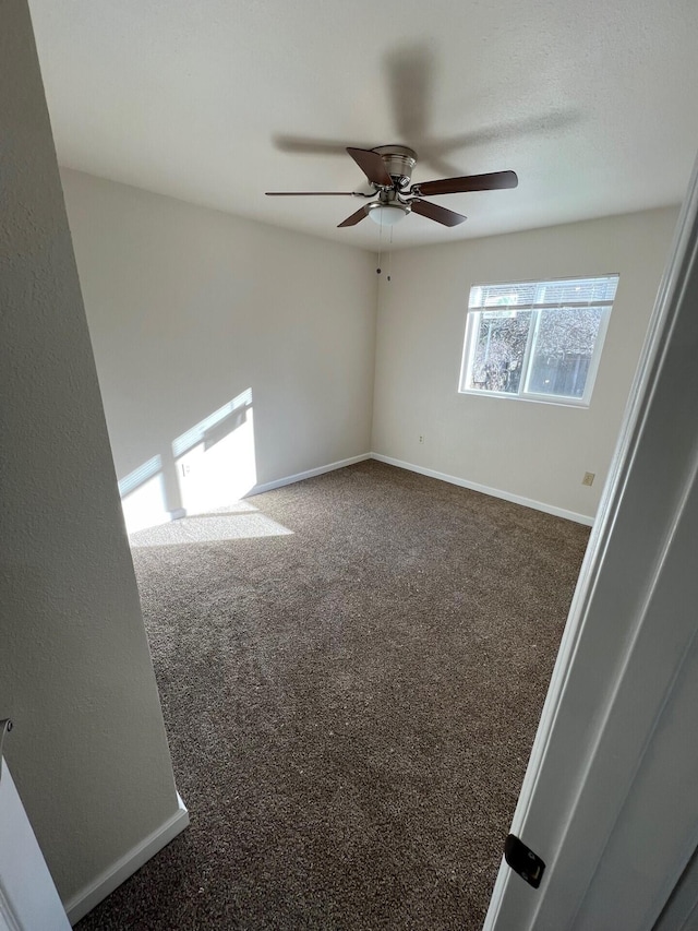 unfurnished room with ceiling fan and dark colored carpet