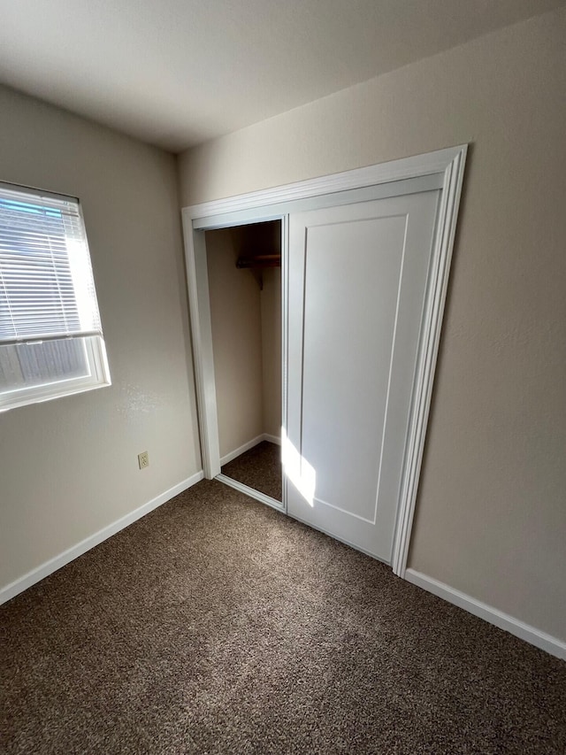 unfurnished bedroom with a closet and dark colored carpet