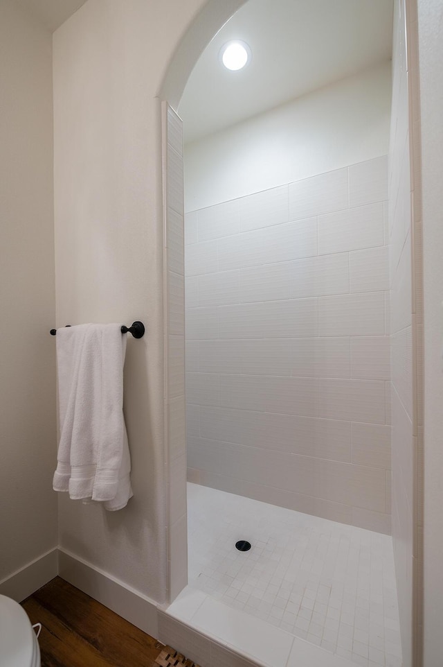 bathroom featuring hardwood / wood-style flooring, tiled shower, and toilet