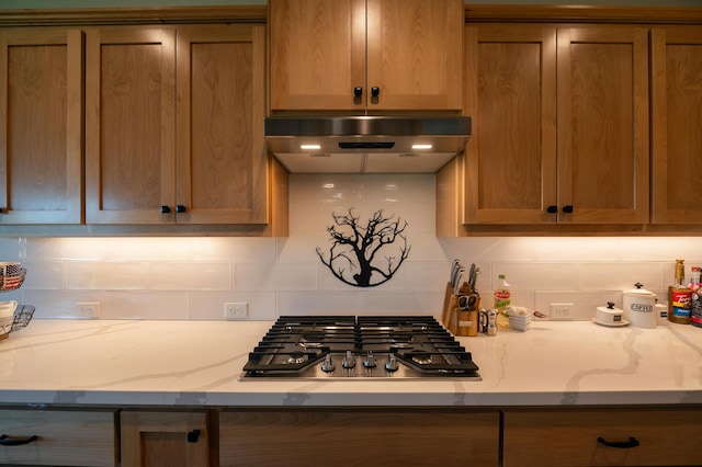 kitchen with stainless steel gas stovetop, tasteful backsplash, and light stone counters