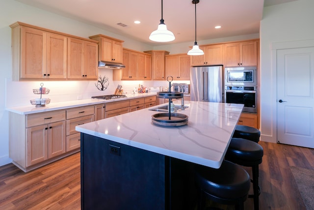 kitchen featuring a kitchen island with sink, light brown cabinetry, decorative light fixtures, and appliances with stainless steel finishes