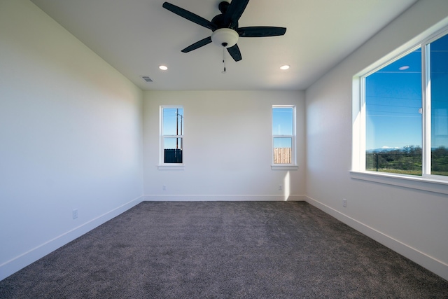 empty room with dark colored carpet, ceiling fan, and a wealth of natural light