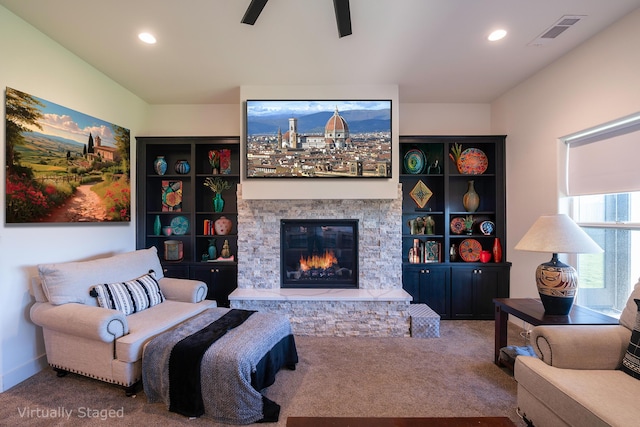 carpeted living room featuring a stone fireplace and ceiling fan