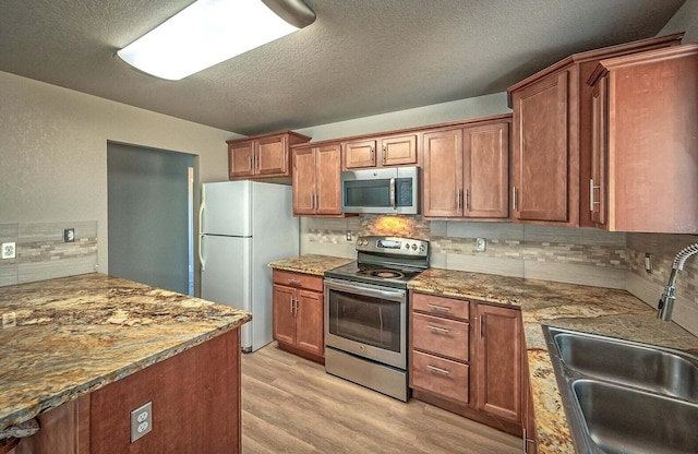 kitchen with stone countertops, tasteful backsplash, sink, stainless steel appliances, and light hardwood / wood-style flooring