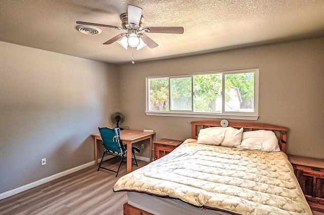 bedroom with ceiling fan, wood-type flooring, and a textured ceiling